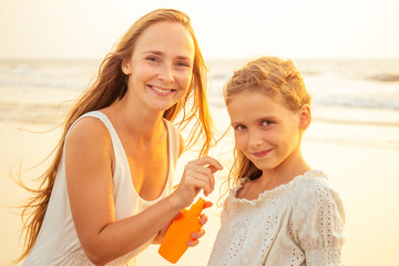 mother and teenager daughter using sunscreen on the beach