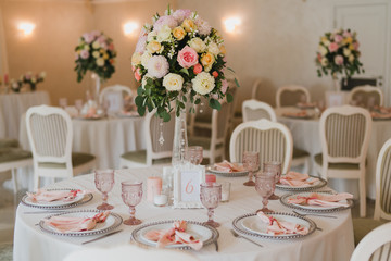 Coziness and style. Modern event design. Table setting at wedding reception. Floral compositions with beautiful flowers and greenery, candles, laying and plates on decorated table.