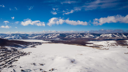 Fototapeta na wymiar Aerial; drone panoramic view of winter mountain landscape with blue sky and clouds; sunny day in russian countryside; snow fields and mixed forest with birches and pine trees; local ski resort Bannoe