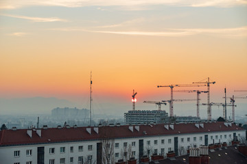 Fototapeta na wymiar Sunset over a construction site in the south of Vienna - sun touching the horizon behind a crane.