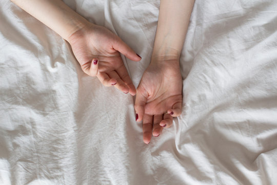 young woman's hands with dark red nail polish in bed with white sheets	
