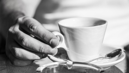 Fototapeta na wymiar Hand of man hold coffee or coffe cup at cafe. Cup of coffee. Cappuccino and black espresso coffe cup. Coffee drink. Close up of a man hands holding a hot coffe cups. Black and white.