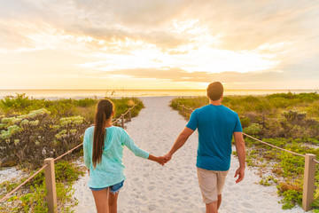 Happy young couple in love walking on romantic evening beach stroll at sunset. Lovers holding hands...