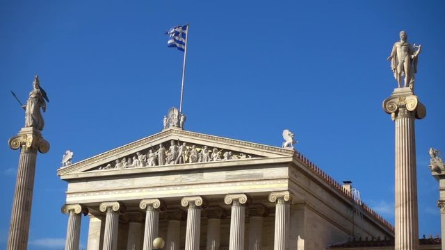 Slow Motion video from iconic neoclassic Academy of Athens facade with Greek flag waving slowly, Athens historic center, Attica, Greece        