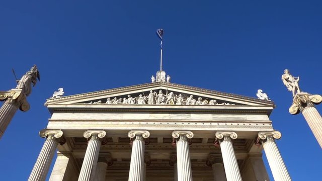 Slow Motion video from iconic neoclassic Academy of Athens facade with Greek flag waving slowly, Athens historic center, Attica, Greece        
