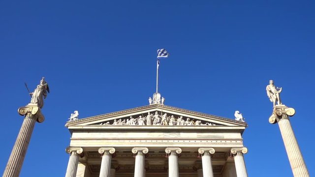Slow Motion video from iconic neoclassic Academy of Athens facade with Greek flag waving slowly, Athens historic center, Attica, Greece        