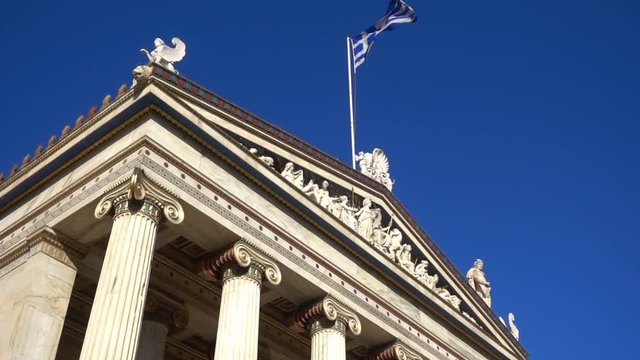 Slow Motion video from iconic neoclassic Academy of Athens facade with Greek flag waving slowly, Athens historic center, Attica, Greece        