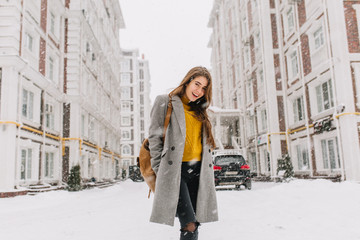 Fashionable young woman in coat with backpack walking on street in big city in snowing time....