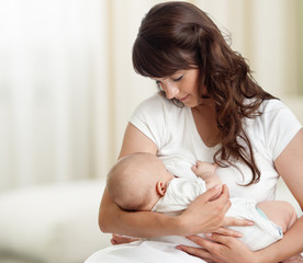 Young mother feeding breast her baby at home in white room - 250585687