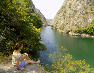 A girl sitting on a rock looking out over the cliff of Matka canyon and mountain river