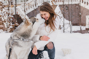 Portrait cute lovely moments of husky dog kissing fashionable young woman outdoor in snow. Cheerful mood, winter holidays, snow time, real friendship, animals love