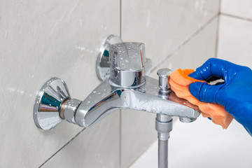 Close-up of the shower faucet and showerhead cleaning process from lime scale, white chalk sediment and stains using a commercial soap scum remover. Bathroom cleaning and disinfection