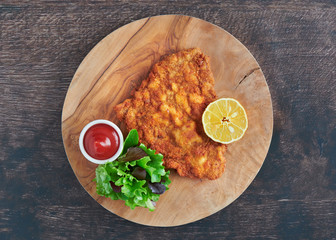 Original Wiener Schnitzel vom Kalb mit Salat und Zitrone zum Essen auf einem Holzbrett 