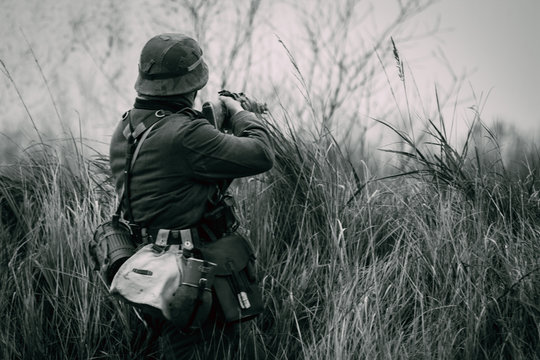 A soldier of the German army Wehrmacht during the Second World War shoots at the enemy from behind the shelter in full growth. Black and white photo