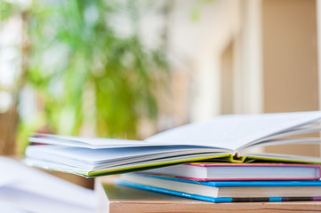 Open book is lying on books with colored covers on a wooden surface.