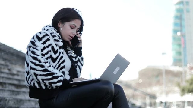 Slow motion shot of serious young woman talking on phone. Thoughtful businesswoman with laptop on her knees talking on smartphone. Business and technology concept