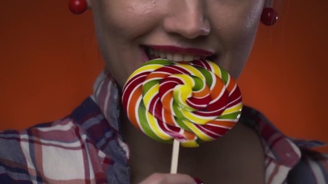 Close up of a cute lady with red lipstick biting on a colorful lollipop