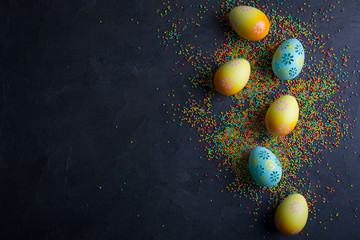 Easter holiday background with eggs. Top view of colorful painted chicken eggs and sugar sprinkle dots on black