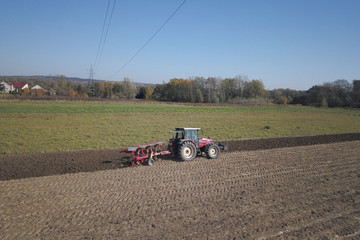 A farmer on a red tractor with a seeder sows grain in plowed land in a private field in the village...