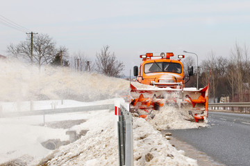 A large car with a plow clears the road from snow. Orange cargo special equipment is struggling...