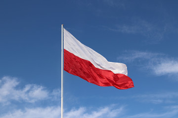 White-red horizontal flag on a flagpole developing in the wind against a blue sky with light clouds. Symbol of the Polish state
