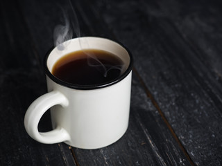 White mug of hot coffee with steam on wooden table