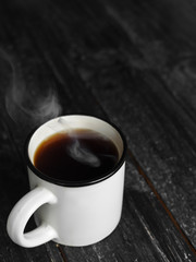 White mug of hot coffee with steam on wooden table