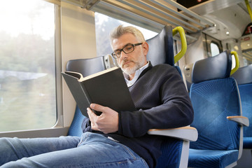 Mature man reading book while traveling on a train