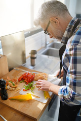 Cheerful mature man in kitchen preparing dish