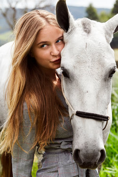 Gorgeous girl kissing her pet pony, looking away