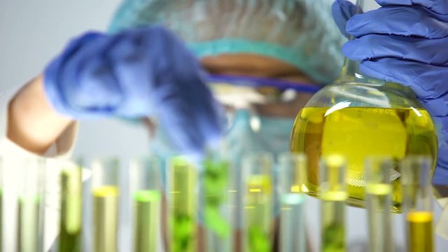 Biochemist dripping yellow substance into test tube with green plant, extraction