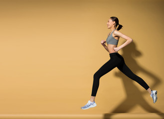 Asian slim Fitness woman exercise warm up stretch spring jumps legs, studio lighting yellow beige mustard background sun shadow copy space, concept Woman Can Do athlete Sport 6 packs
