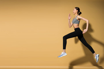 Fototapeta na wymiar Asian slim Fitness woman exercise warm up stretch spring jumps legs, studio lighting yellow beige mustard background sun shadow copy space, concept Woman Can Do athlete Sport 6 packs