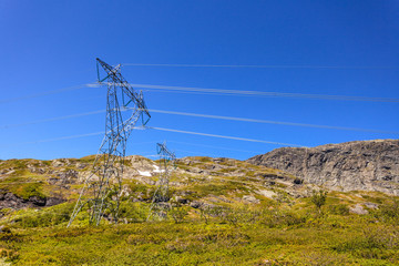 Power line voltage tower in mountains against blue sky
