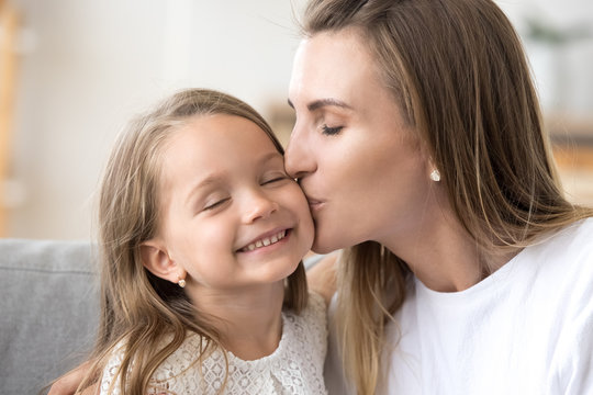Loving young mother kissing little smiling daughter on cheek
