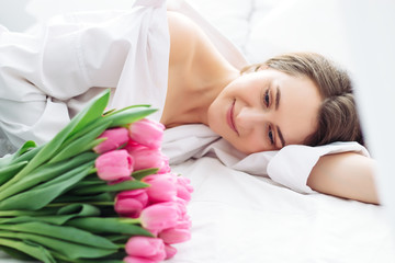 Obraz na płótnie Canvas young woman sleep on the white bed. Pink tulips for her at womans day as surprise