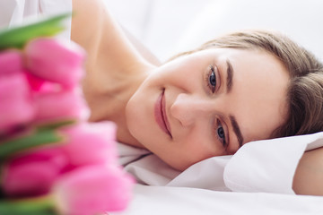 Fototapeta na wymiar young woman sleep on the white bed. Pink tulips for her at womans day as surprise