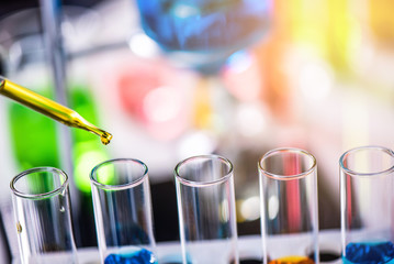 Using dropper sampling oil or chemical liquid drop to test tube with lab glassware in laboratory background, science or medical research and development concept