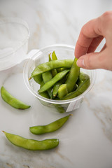 Frau isst portion grüne, japanische Edamame Sojabohnen in Plastik Lieferdienst Take Away Schale