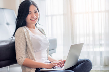 Fototapeta premium Beautiful attractive young Asian woman using laptop at living room in the morning 