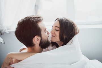 beautiful young happy couple covered in blanket embracing and looking at each other at home