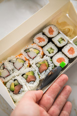 Frau isst Maki und Inside Out California Sushi vom Lieferdienst mit Lachs, Surimi, Avocado, Gurken mit Ingwer, Wasabi und Soja Soße in Einweg Bento Box Verpackung