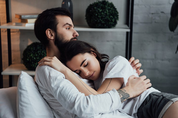 Obraz premium attractive young tattooed couple embracing while lying in bed at home