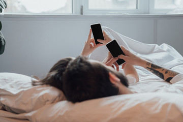 young couple lying in bed and using smartphones with blank screen