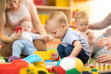 Nursery babies playing with adults in day care center - obrazy, fototapety, plakaty