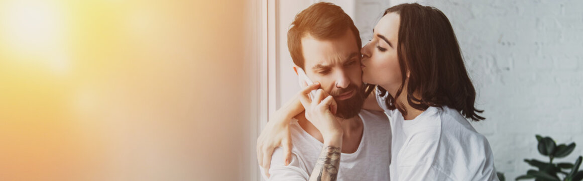 beautiful woman kissing man talking on smartphone at home with copy space and sunlight