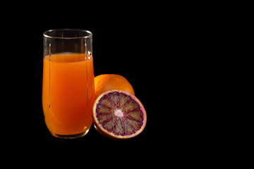 Glass of juice, knife and cut red oranges on a black background.