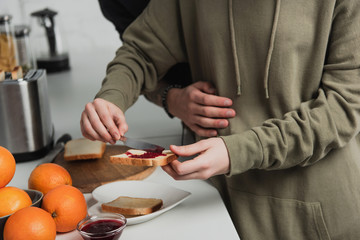 cropped view of couple preparing toasts with jam during breakfast in kitchen