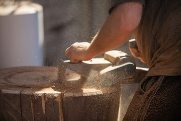 Carpenter working with electric planer on wooden stump outdoors