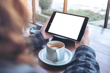 Mockup image of woman's hands holding black tablet pc with blank screen with coffee cup on wooden table in cafe